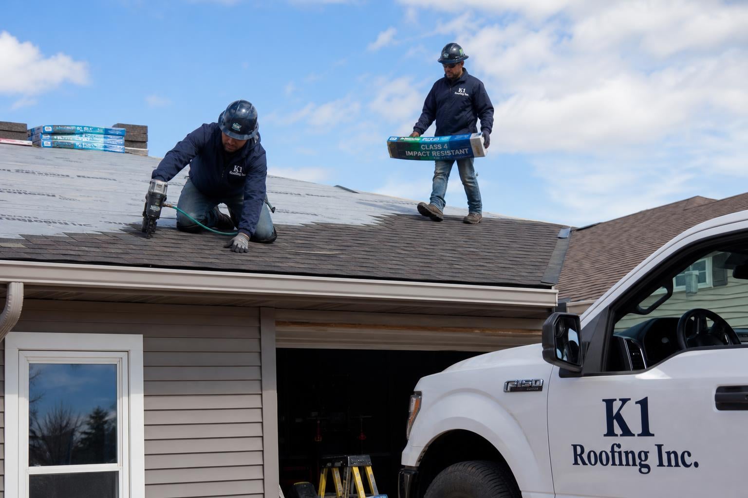 K1 Roofing Inc. crew installing Class 4 impact-resistant asphalt shingles on a Rapid City SD residential roof with a K1 Roofing Inc. branded pickup truck visible in the driveway
